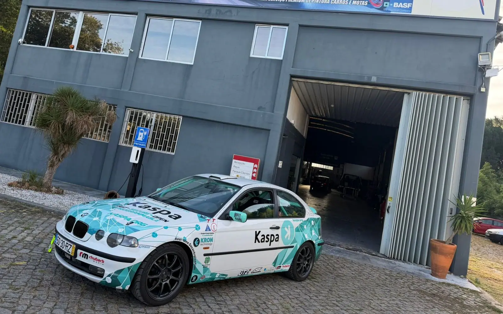 The finished white and teal Kaspa rally BMW parked on the cobbles outside the Auto Souto workshop