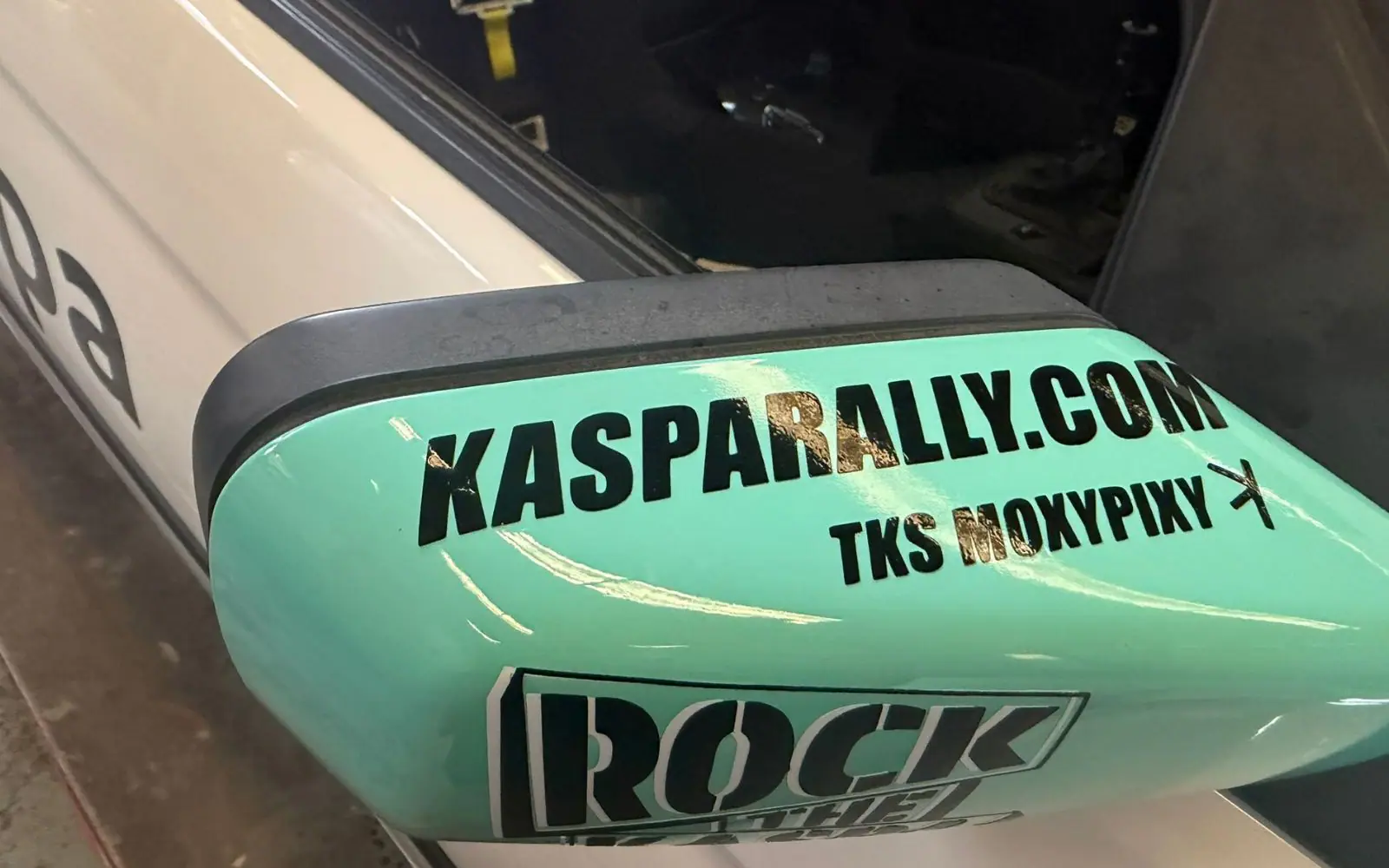 Close-up of the teal door mirror lettered KASPARALLY.COM