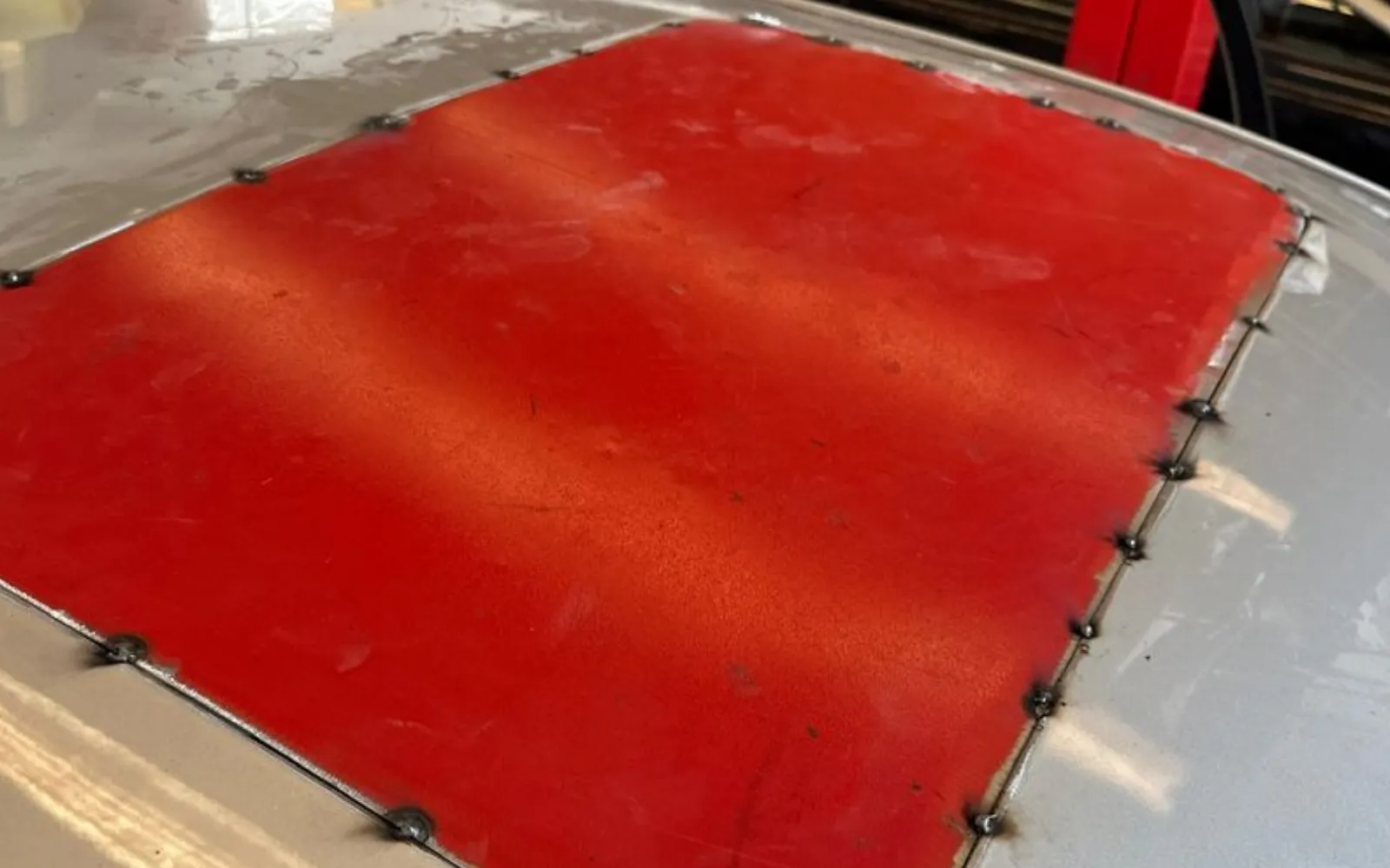A red panel bonded and pinned into the roof of the silver BMW where the sunroof was removed