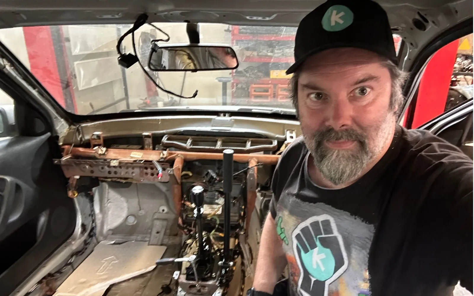 The driver inside the stripped shell, dashboard removed and the wiring loom exposed across the bulkhead