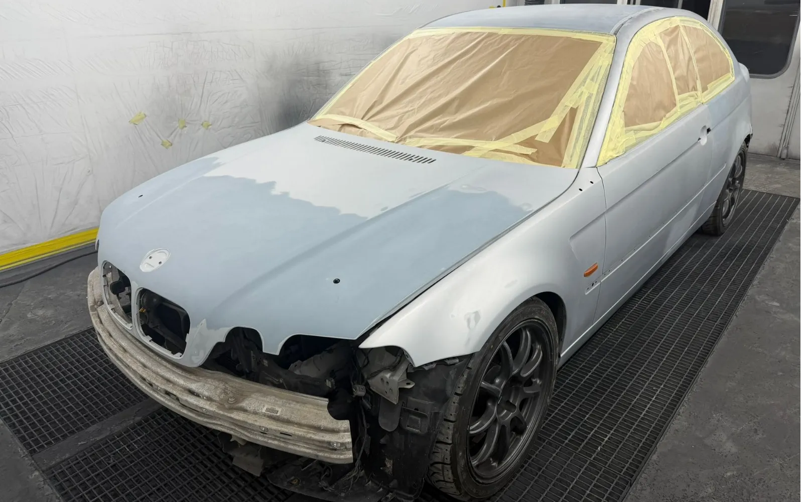 The BMW shell in the spray booth coated in primer, with the windscreen, side windows and roof masked off in tape and paper