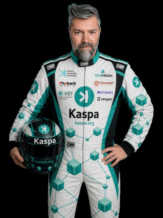 The Kaspa Rally driver in a white and teal Kaspa race suit, holding a matching helmet, against a black studio background